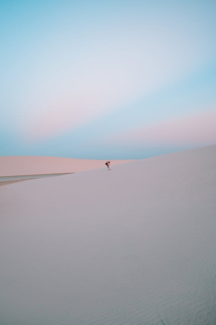 A lone individual in the vast Atins desert dunes at sunset, capturing a serene moment.
